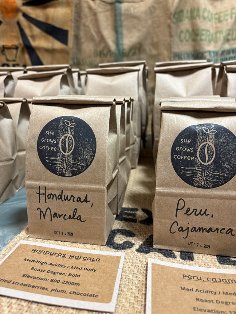 She Grows Coffee fresh roasted coffee beans being displayed in their recycled kraft bags, including Peru and Honduras.